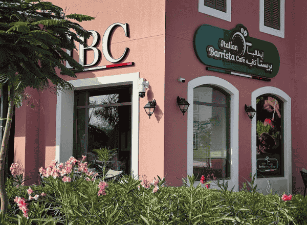 Front view of Italian Barrista Cafe, an Italian restaurant in Salalah located on Al Sultan Taymoor Street, featuring a pinky exterior and greenery with IBC Brand name.