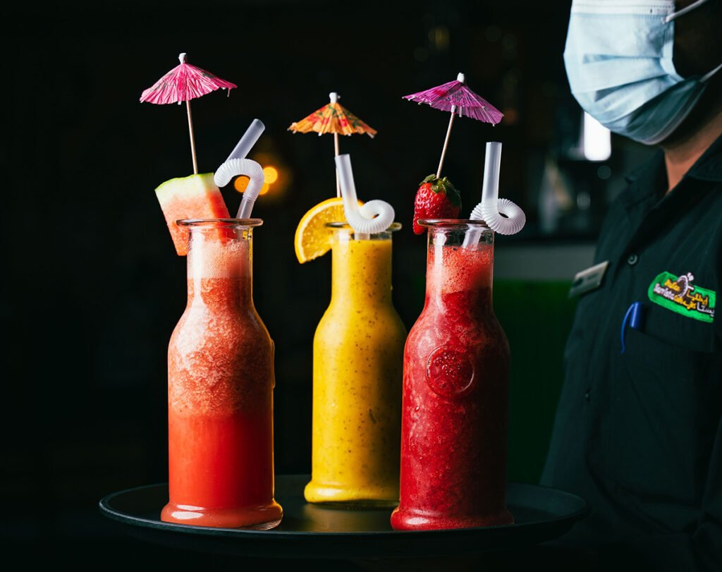 Three vibrant tropical mocktails with fruit garnishes and umbrellas served at an Italian restaurant